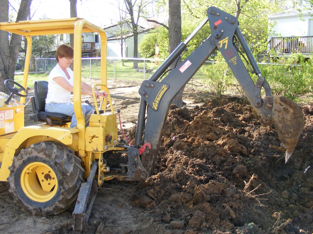 Woman using a backhoe to dig a Koi pond